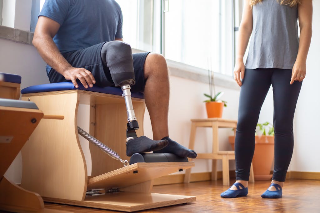 Man using prosthetic leg during rehabilitation exercise with trainer in gym setting.